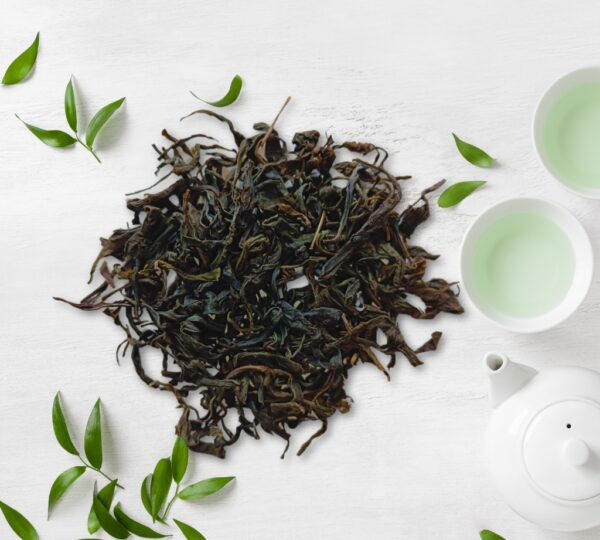 Pile of Bonobithi Health Food loose Orthodox Green Tea leaves with tea cups and teapot on white background.